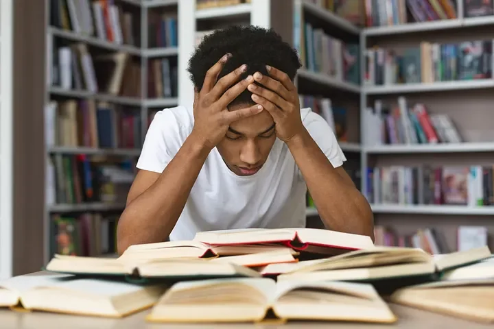 Student stressed with books in a library, representing the challenge of predicting what to study